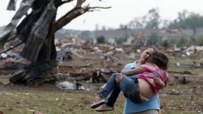 A woman carries a child through a field near the collapsed Plaza Towers Elementary School in Moore