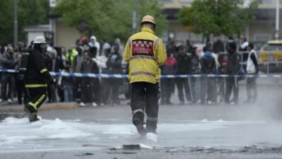 People watch as firemen extinguish burning cars in the Stockholm suburb of Rinkeby