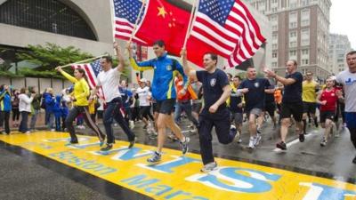 Runners holding three American flags and one Chinese cross the finish line of the Boston Marathon (25 May 2013)