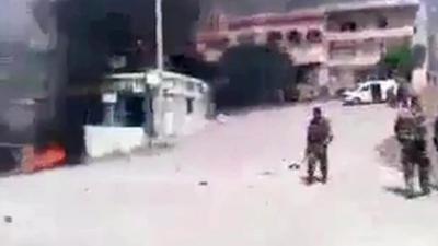 Still from video showing fighter in square, fires burning
