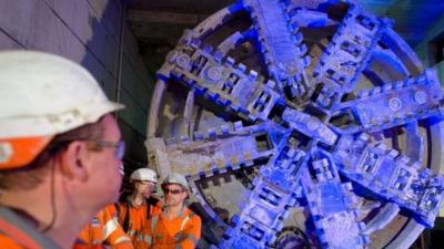 Crossrail construction workers stand near to one of the 1,000 tonne tunnel boring machines to mark the breakthrough into the Canary Wharf station