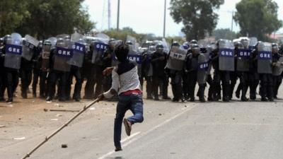 A protester throws a stone at riot police during clashes in front of a factory owned by Sabrina