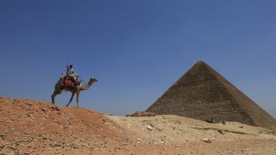 A man rides a camel past a pyramid at Giza