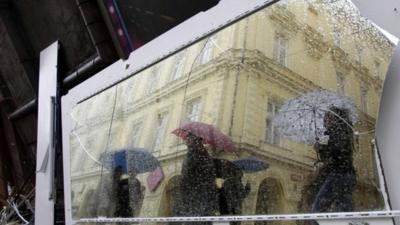 People holding umbrellas are reflected in a broken mirror taken out of a house affected by the floods, Prague