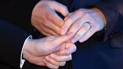 Two men holding hands with wedding rings