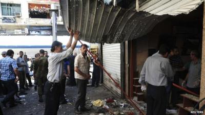 People gather at the site after bombs exploded close to a police post in the central Marjeh Square in Damascus