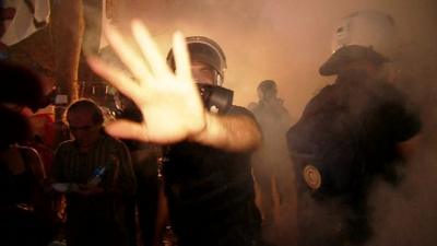 Riot police waving away camera through fog of tear gas