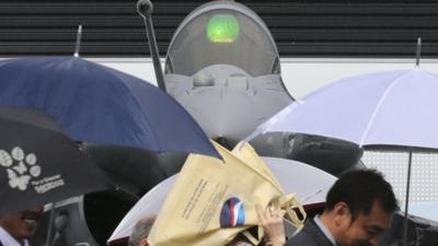 Visitors walk in front of a Dassault Rafale fighter on the first day of the rain-soaked 50th Paris Air Show, at Le Bourget airport near Paris