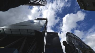 Man walking through City of London with skyscrapers above his head