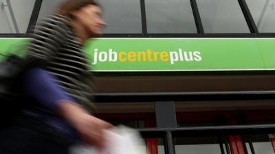 A woman walks past a Job Centre sign