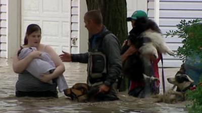 Woman with child and several dogs being helped through flood water