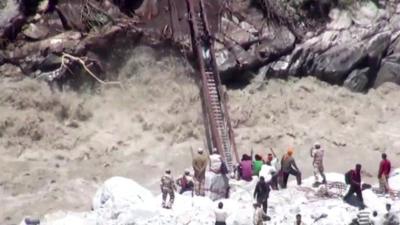 Pilgrims cross a rope bridge over a flooded river