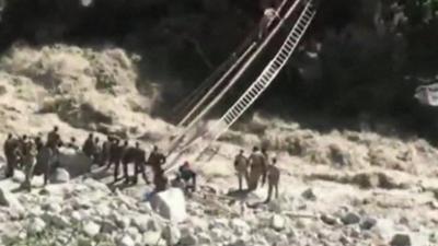 Turbulent river with rescuer climbing makeshift ladder across