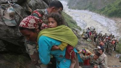 Soldiers assist a woman carrying a child on her back during rescue operations in Govindghat in Uttarakhand on June 23, 2013