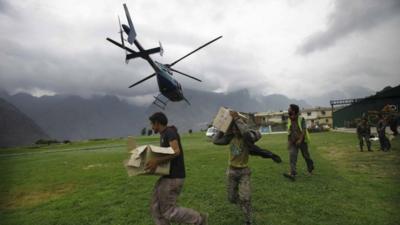 Indian civilians get ready to load relief material for flood affected victims on a helicopter at a makeshift helipad at Joshimath, in northern Indian state of Uttarakhand,