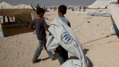 Two young boys carrying a tent in a refugee camp