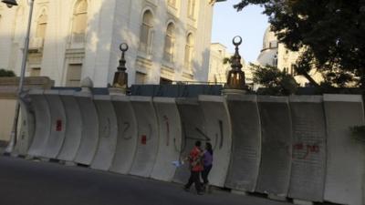 People walk in front of new concrete barricades erected to prevent any attacks at El-Thadiya presidential palace in Cairo