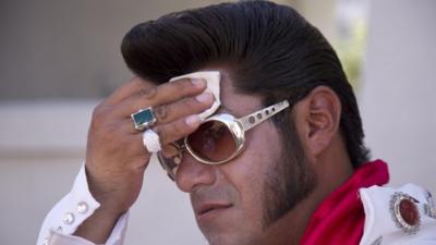 Elvis impersonator Cristian Morales wipes sweat from his brow while standing out on The Strip posing for photos with tourists