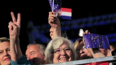 A woman makes victory sign as she holds the EU flag during the celebration of the accession of Croatia to the EU in Zagreb