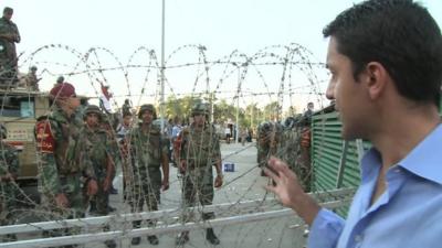 The BBC's Aleem Maqbool stands in front of barbed wire at a pro-Morsi march