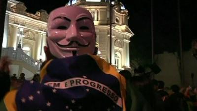 Protester wearing Guy Fawkes mask and Brazil flag