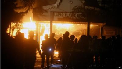 Police officers stand outside Tanjung Gusta prison, on fire