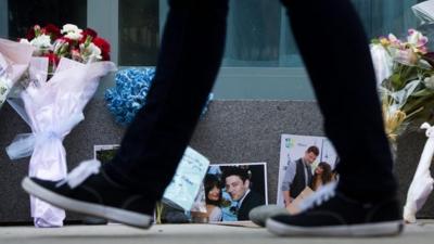 A pedestrian walks past photographs and flowers placed at a memorial for Canadian actor Cory Monteith outside the Fairmont Pacific Rim Hotel in Vancouver