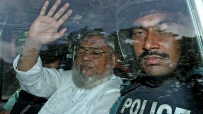 Ali Ahsan Mohammad Mujahid (left) waves from a police vehicle as he is transported to the central jail following his court verdict on 17 July