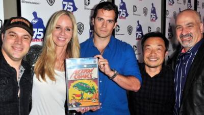 DC Comics figures with Henry Cavill, holding the first issue of Action Comics, in which Superman debuted