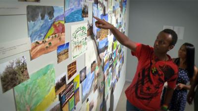 Ethiopian refugee points at artwork on the wall.