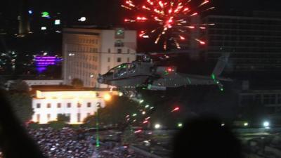 An Apache helicopter flies over Tahrir Square as a firework explodes