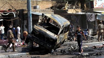 People and security forces inspect the site of a car bomb explosion in Basra