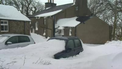 Car part-buried by snow drifts outside house