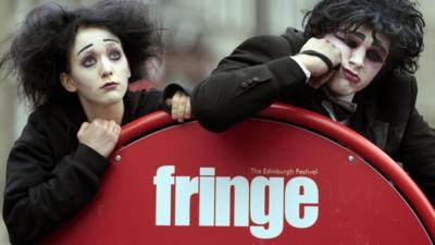 Actors pose by a sign for the Edinburgh Fringe Festival