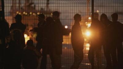 A group of people in shadow at a fence in Calais