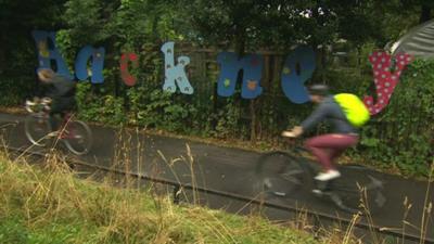 Cyclists riding past a Hackney sign