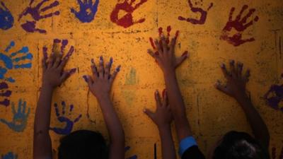 Young Syrian refugees touch colourful handprints on a mural that they made on one of the public bathrooms at Zaatari refugee camp