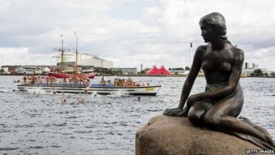 Little Mermaid statue and 100 'mermaids' jumping off boat behind it