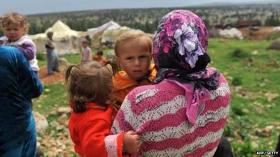 A Syrian woman carries her children near their makeshift refugee camp at the mountains of the city of Afrin, on the Syria-Turkey border, on March 28, 2013