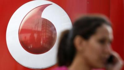 A woman talks on her mobile phone as she walks past a Vodafone store in London