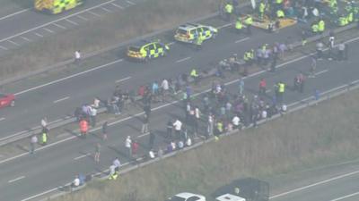 Aerial shot of people standing by the side of the road and emergency vehicles