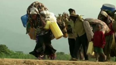 DRC refugees walking on a dusty road, carrying their belongings with them.