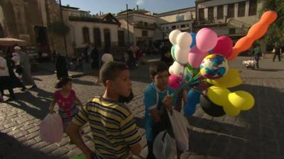 Children hold balloons on a street in Damascus