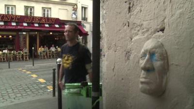 French artist Gregos walks past one of his face sculptures in Paris