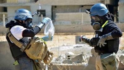 Members of the UN investigation team take samples from sand near a part of a missile that is likely to be one of the chemical rockets according to activists