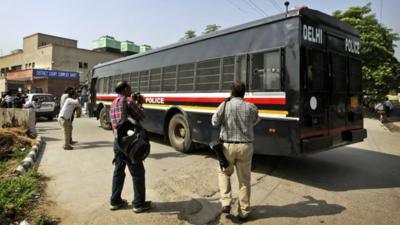 Photographers gather by a van, carrying four men accused in the fatal gang rape of a young woman