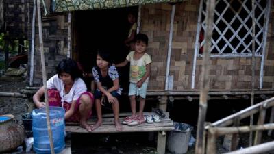 A family sitting outside their bamboo house built in the compound of a Buddhist monastery and meditation centre, in Yangon, Myanmar