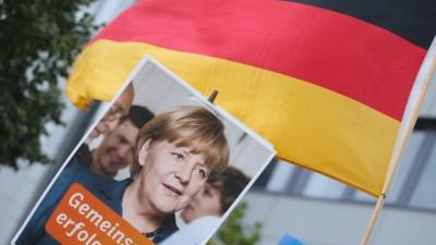 Angela Merkel supporters hold up a German flag and advertisement