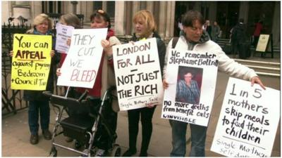 Women stand outside parliament with banners protesting the 'bedroom tax' policy