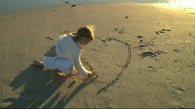 Girl drawing heart in sand